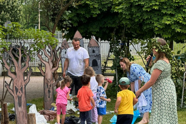 Na zdjęciu grupa osób - dorośli i dzieci. Dzieci sprzątają śmieci z ziemi.