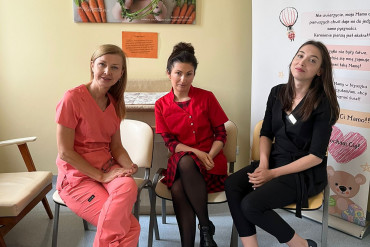 Na zdjęciu siedzą 3 kobiety uśmiechając się w stronę aparatu
