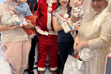 Na zdjęciu z grupie uśmiechając się wprost do aparatu stoją dwie mamy małych pacjentów, trzymając na rękach swoje małe dzieci, obok nich stoją również pracownicy przebrani za Diabła, Aniołka i św. Mikołaja