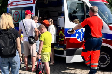 Zdjęcie przedstawia karetkę do której ustawiają się ludzie. Drzwi karetki trzyma pracownik szpitala.