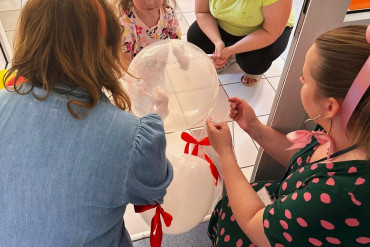 Kobiety kucają na przeciwko uśmiechniętej dziewczynki, Obok nich, przy dziewczynce kuca mama.